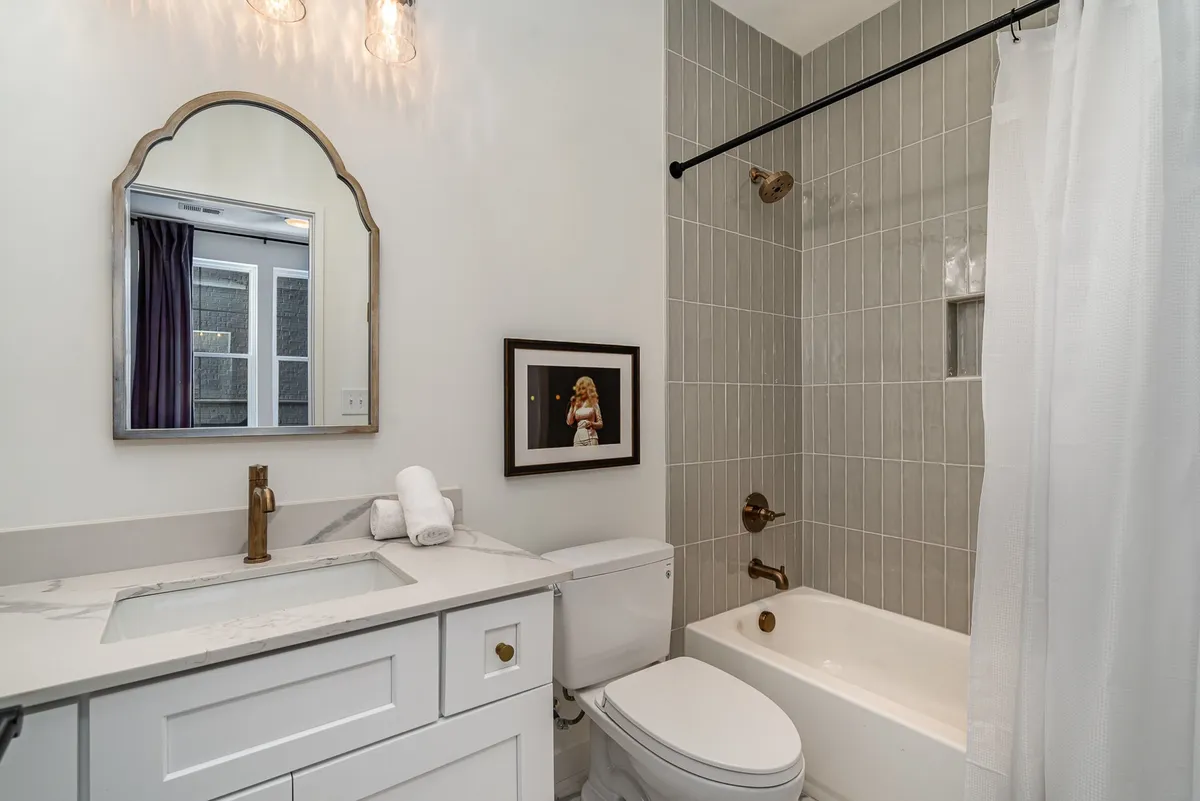 A modern bathroom interior with a mirrored vanity, gold fixtures, textured tiles, and framed artwork. The space feels fresh and inviting, ideal for both relaxing baths and efficient morning routines.
