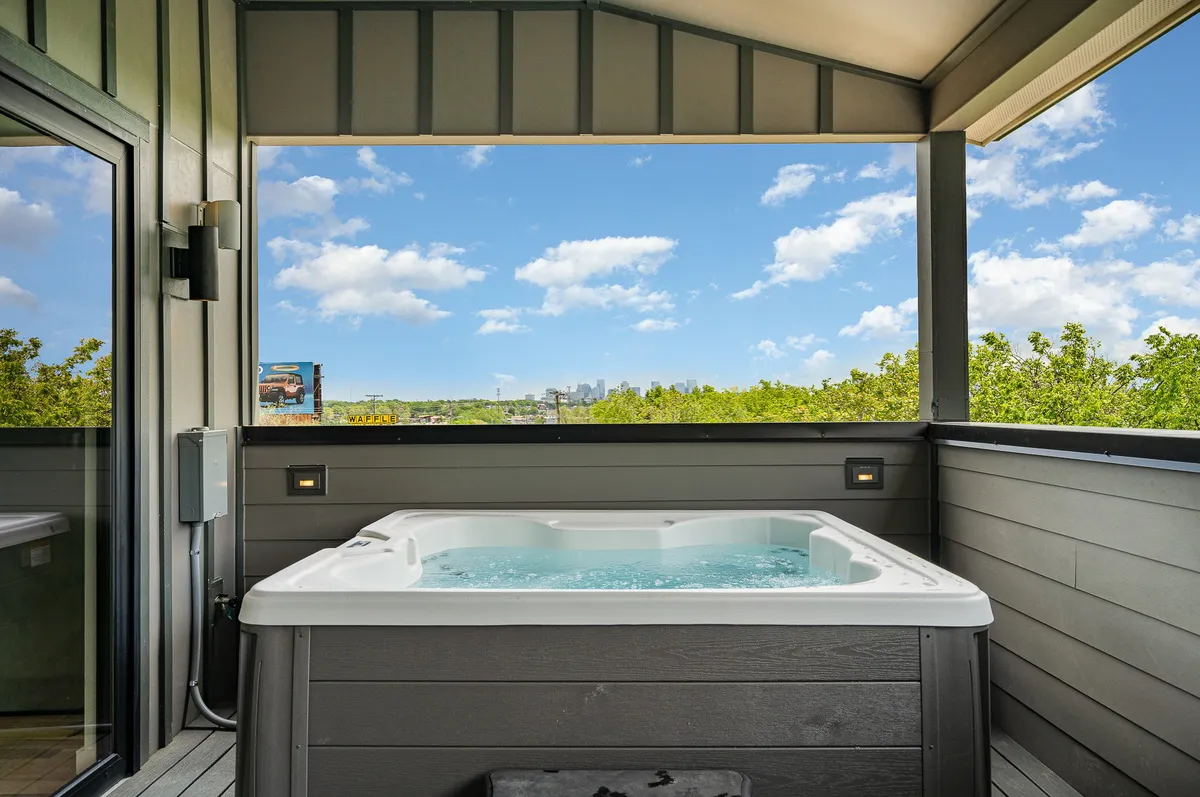 A private outdoor hot tub set on a deck with lush greenery and the city skyline in the background. The space exudes tranquility and invites relaxation, with ample room for socializing and enjoying the view both day and night.