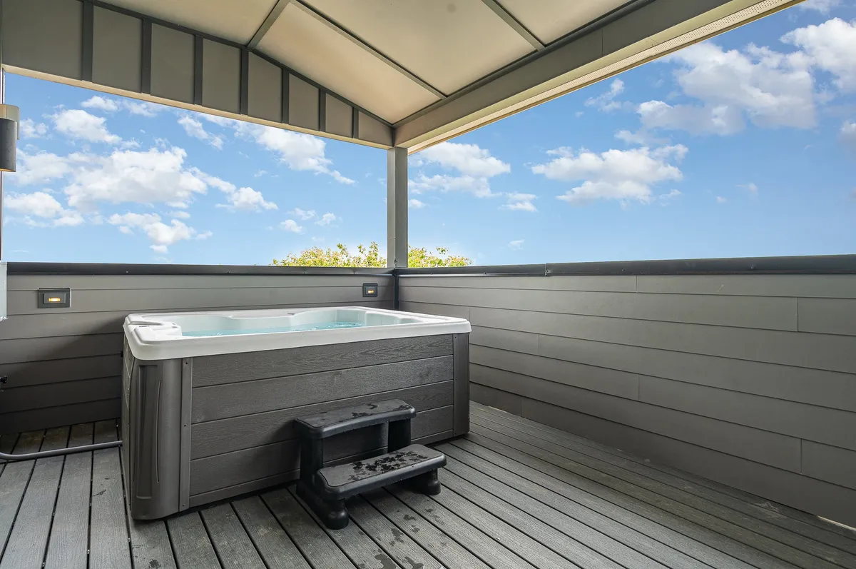 A tranquil exterior view of a hot tub on a private wooden deck, set against an expansive sky. The inviting water and serene setting suggest relaxation and unwinding after a night out.