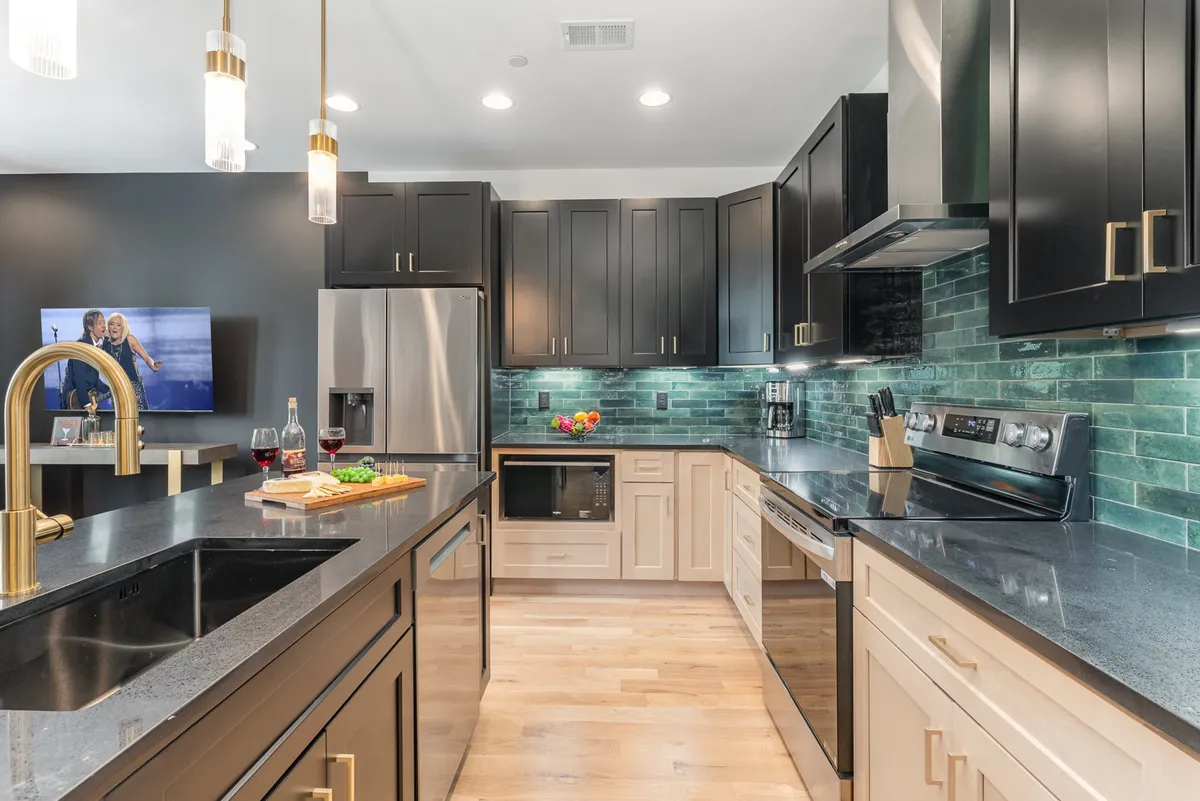 A view of another kitchen featuring an island, stylish cabinetry, backsplash, appliances, and an adjacent dining area. The layout encourages social cooking and hosting, with ample counter space and comfortable seating for guests.